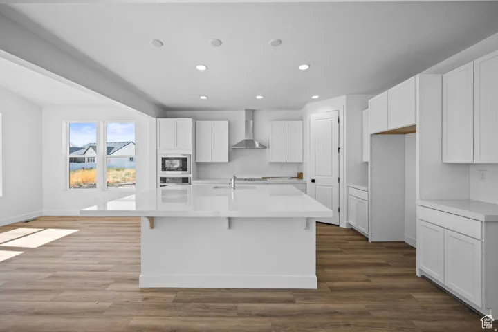 Open-concept kitchen featuring an expansive island, white cabinetry, integrated stainless steel appliances, recessed ceiling lights, and wood-finish flooring. This is not the actual home being built but a representation of the features available in this h