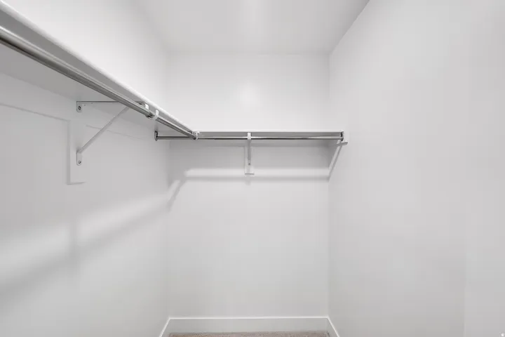 Walk-in closet with white walls, L-shaped shelving, and metal hanging rods. This is not the actual home being built but a representation of the features available in this home. Colors and finishes may differ from those shown.
