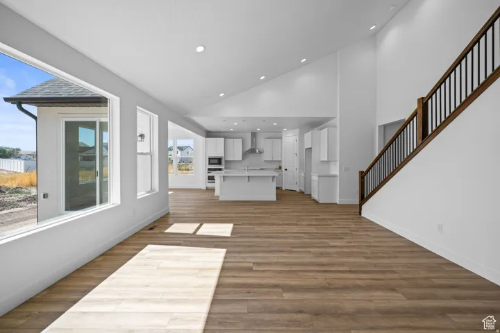 Open-concept main living area featuring wood-finish flooring, high vaulted ceilings with recessed lighting, and a contemporary staircase. This is not the actual home being built but a representation of the features available in this home. Colors and finis
