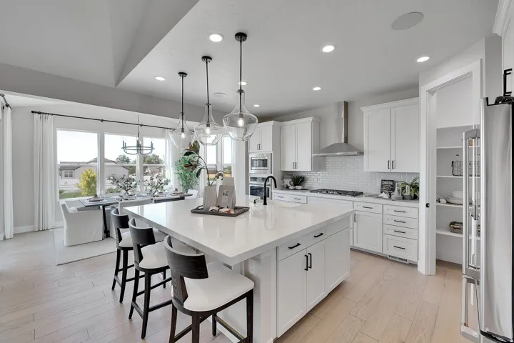 Open-concept kitchen featuring an oversized island with seating, white shaker cabinetry, stainless steel appliances, and wood-finish flooring. This is not the actual home being built but a representation of the features available in this home. Colors and
