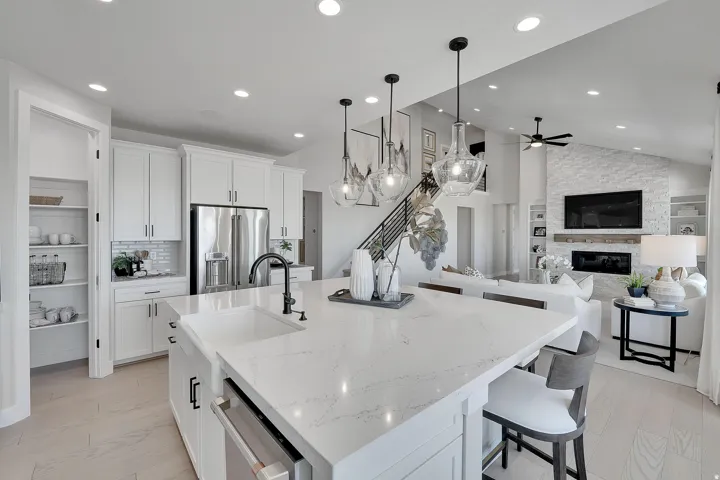 Open-concept living space featuring a spacious kitchen island with a built-in sink, white cabinetry, stainless steel appliances, and wood-finish flooring. This is not the actual home being built but a representation of the features available in this home.