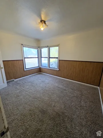 Corner windows providing ample natural light, wall paneling, ceiling-mounted light fixture, and carpeted flooring