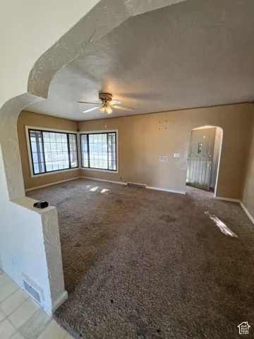Arched entryway leading to a carpeted room with multiple windows, a ceiling fan, and a light-colored wall finish