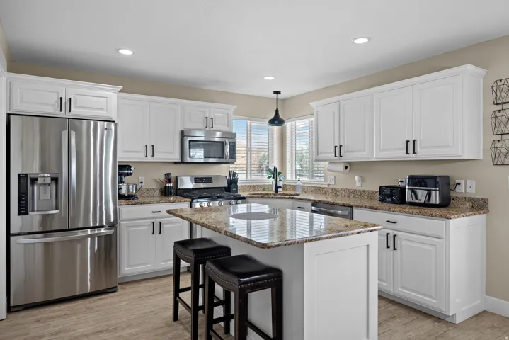 Kitchen featuring granite countertops, white cabinetry with dark hardware, stainless steel appliances, and wood-finish flooring