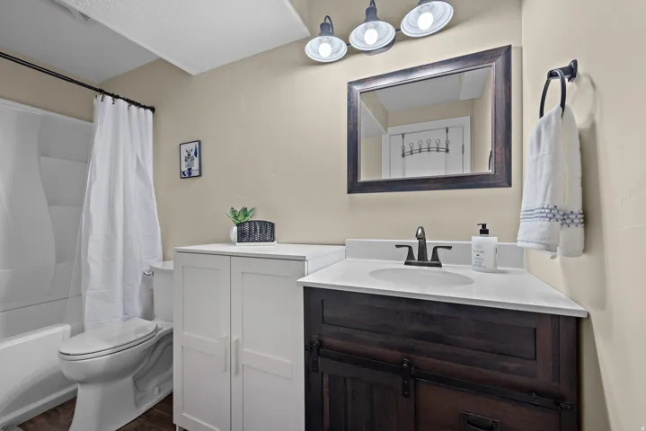 Bathroom featuring a white bathtub with shower, white toilet, and wood-finish flooring