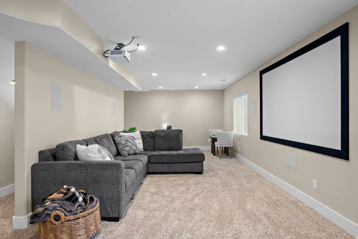 Dedicated media room featuring a large projection screen, mounted projector, recessed lighting, and wall-mounted speakers