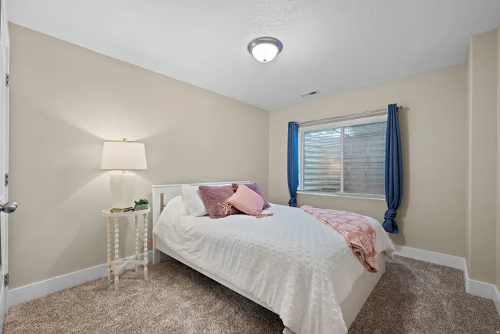 Bedroom featuring light-toned walls, textured carpeting, a window with horizontal blinds, and a semi-flush mount ceiling light fixture