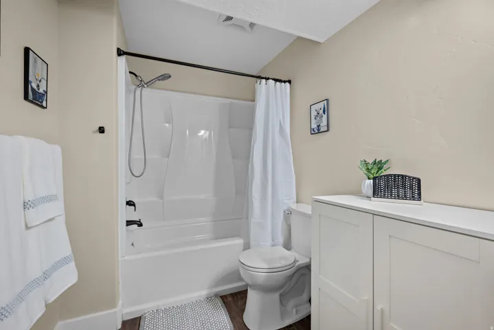 Bathroom featuring a white bathtub/shower combination with black fixtures, a white toilet, and white built-in cabinetry with a countertop