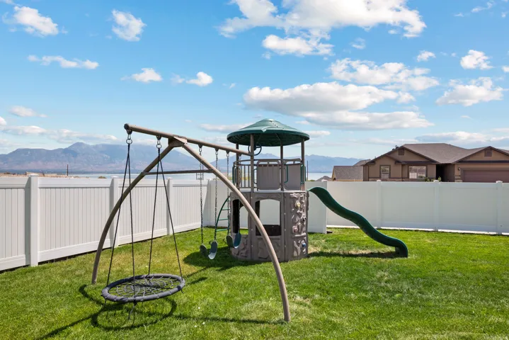 Expansive backyard featuring a lush green lawn, full privacy fencing, and a permanent playset with slide and swings