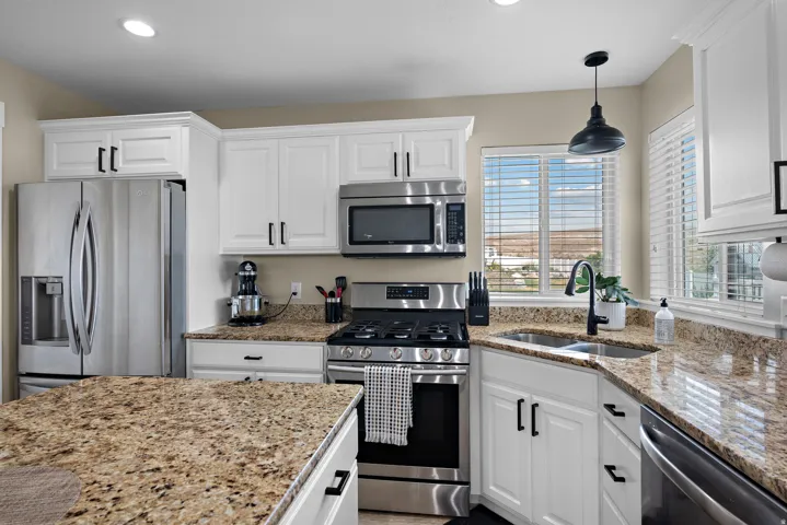 Modern kitchen featuring white cabinetry, granite countertops, stainless steel appliances, a gas range, and a window above the sink