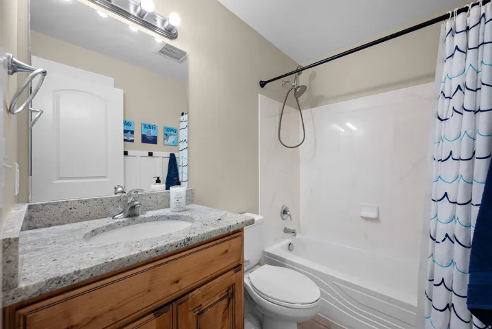 Bathroom featuring a natural wood-finish vanity, light-toned countertop, integrated sink, and a combination shower/tub with white surround