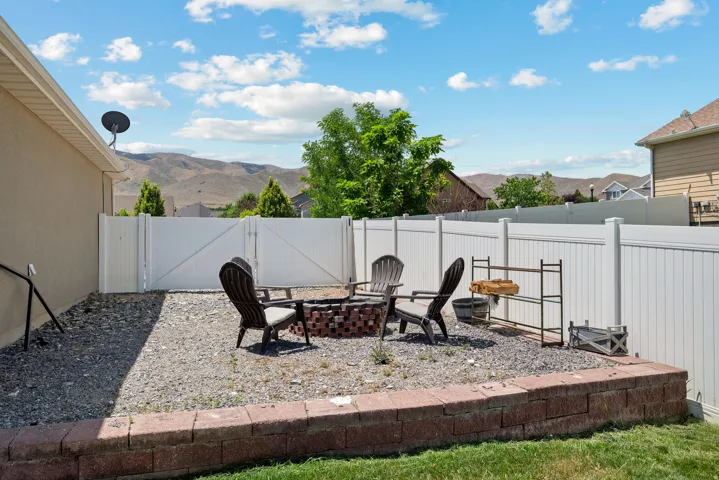 Gravel patio area featuring a brick-built fire pit, a perimeter privacy fence, a retaining wall, and distant mountain scenery