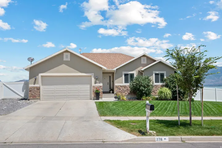 Ranch-style residence featuring a combination stucco and stone facade, an attached two-car garage, concrete driveway, and a front lawn with mature landscaping
