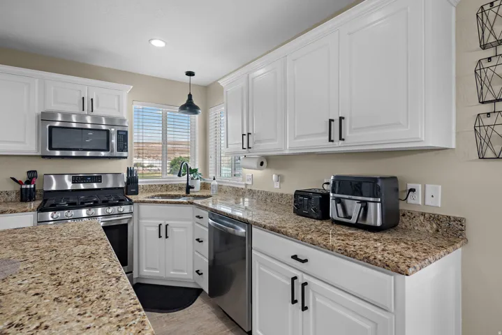 Kitchen featuring white cabinetry with dark hardware, stainless steel appliances, granite countertops, and a window with horizontal blinds