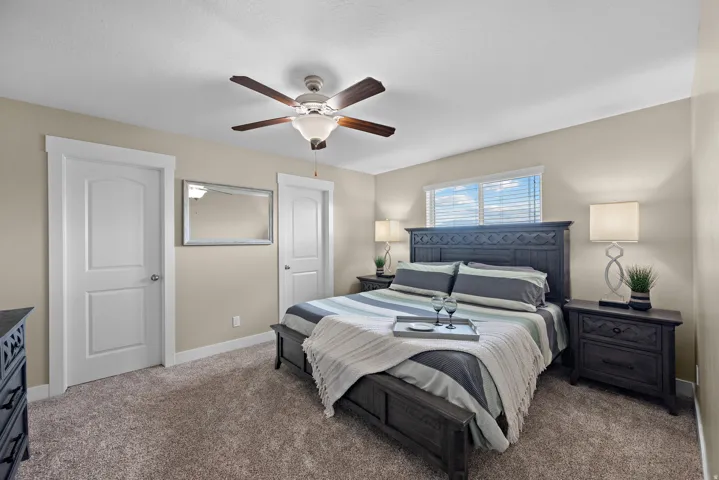 Carpeted sleeping area featuring a ceiling fan with light fixture, window with blinds, and white interior doors