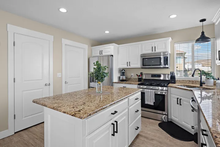 Kitchen featuring a central island with a stone-finish countertop, white cabinetry, stainless steel appliances, and wood-finish flooring
