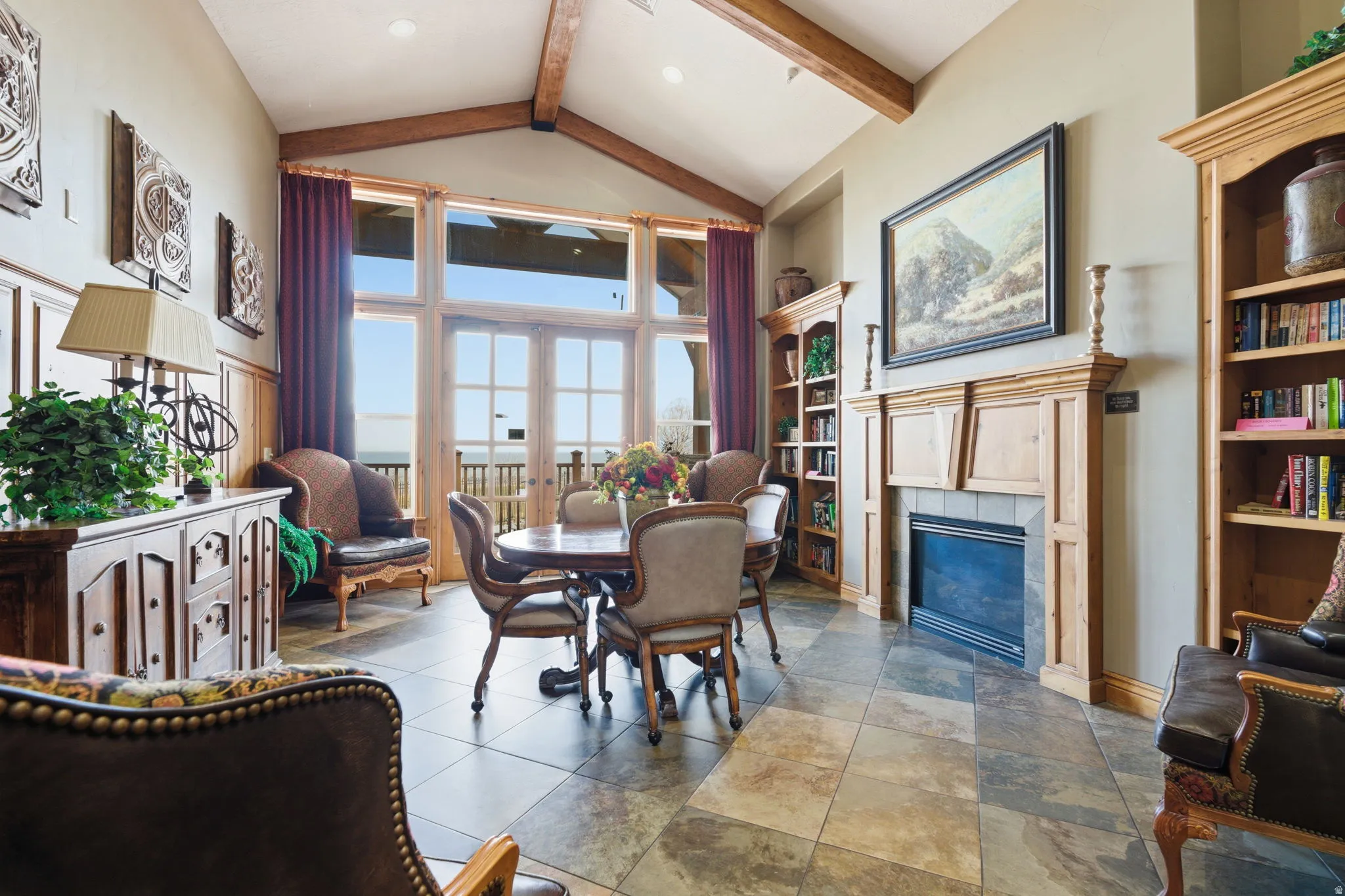 Vaulted ceilings with exposed wood beams highlight this living space featuring extensive window and door openings, providing abundant natural light