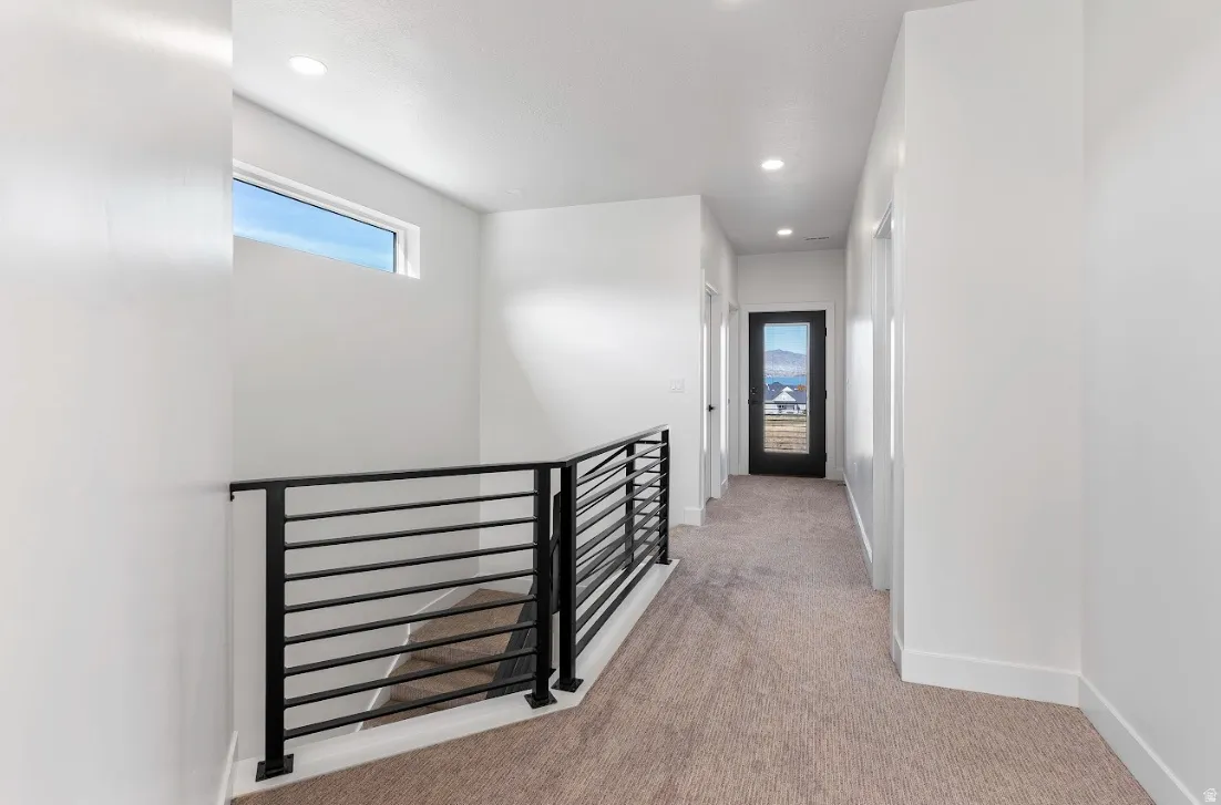 Upper-level hallway featuring a contemporary black metal railing and neutral carpet flooring