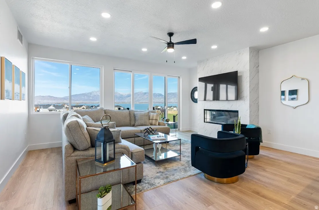 Living area featuring expansive windows, wood-finish flooring, a contemporary fireplace with a stone-finish surround, recessed lighting, and a ceiling fan