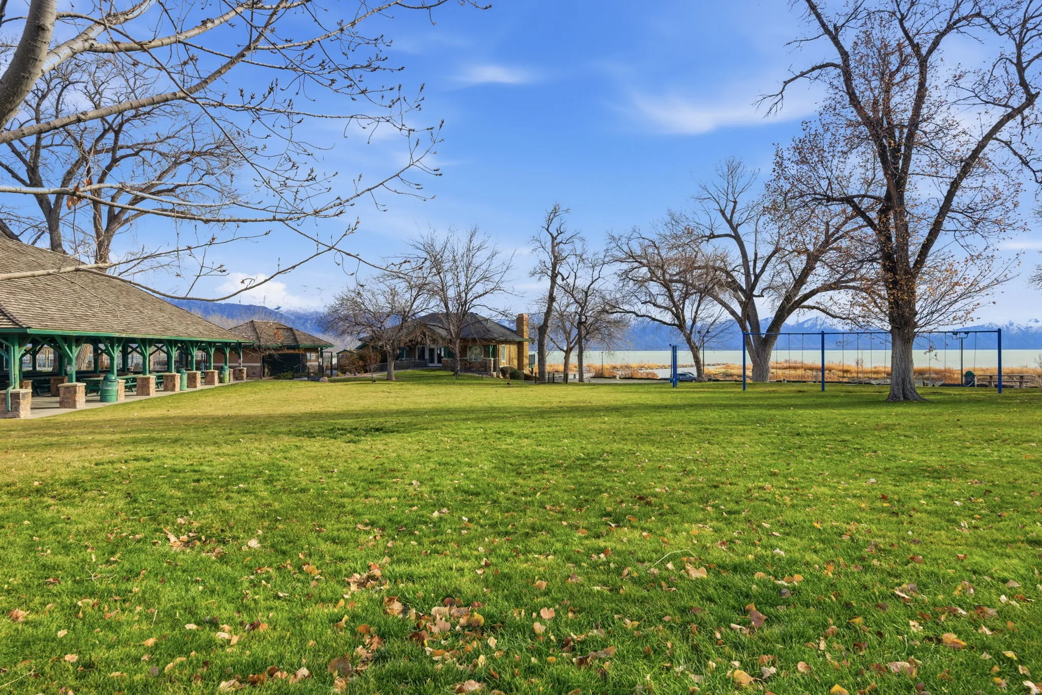 Expansive green lawn fringed by mature trees, featuring a large covered pavilion with stone columns and a shake roof