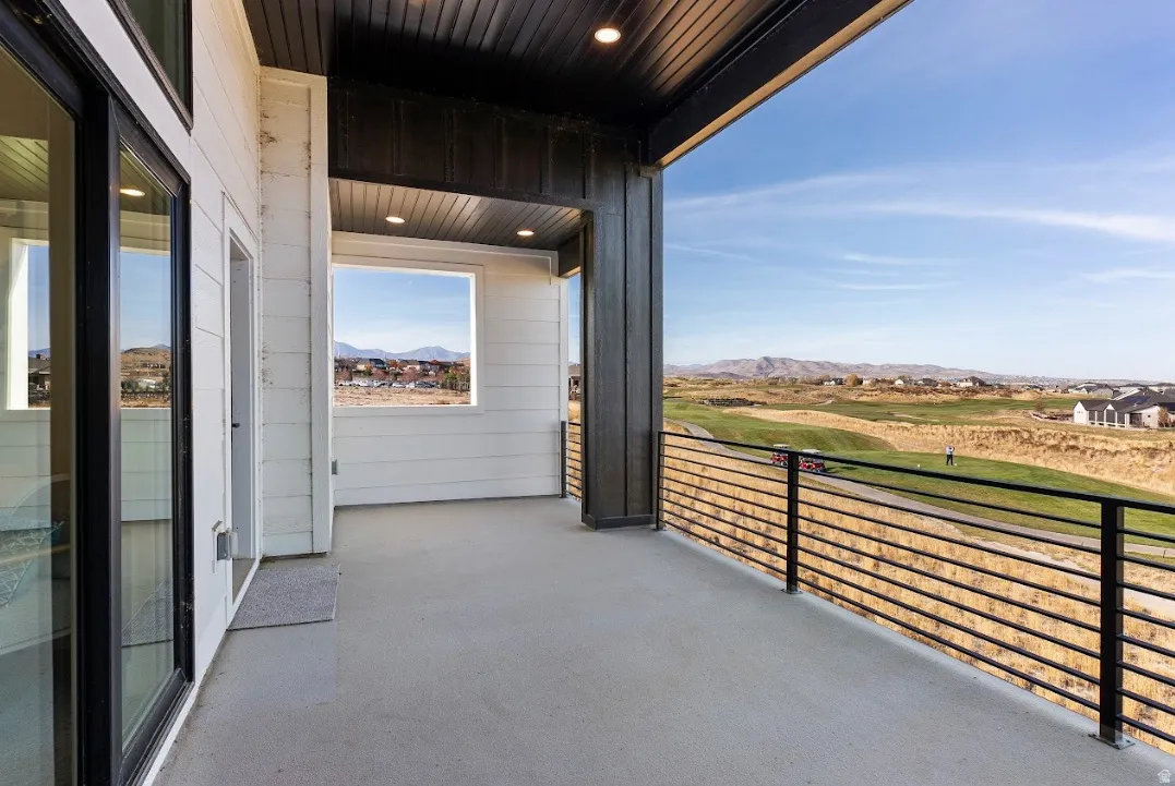 Expansive balcony with concrete flooring, black horizontal railing, and a slatted ceiling with recessed lighting