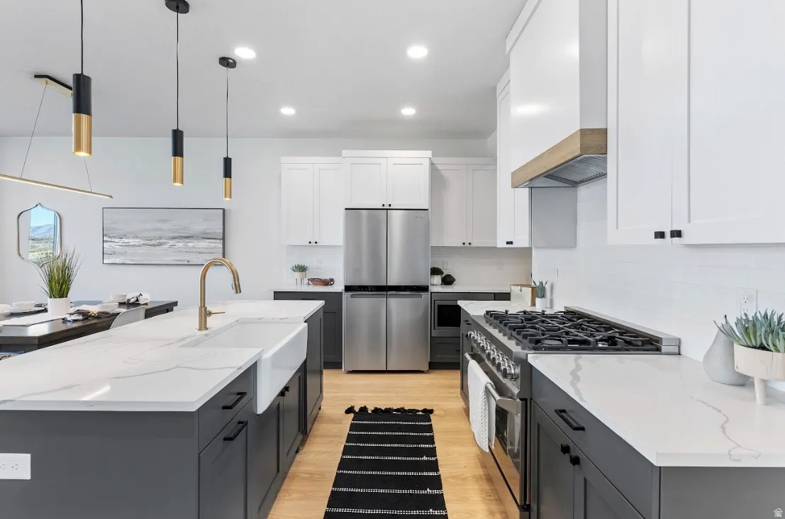 Kitchen featuring a large island with a farmhouse sink and brass faucet, stainless steel appliances, white subway tile backsplash, light wood-finish flooring, and pendant lighting