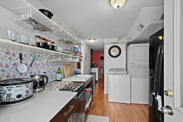 Efficient kitchen area featuring wood-finish flooring, white countertops, built-in shelving, a gas range, and a stacked washer and dryer