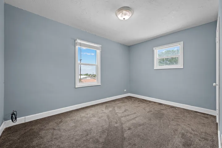 Room featuring two windows, light blue walls, dark gray carpet, white baseboards, and a flush-mount ceiling light fixture