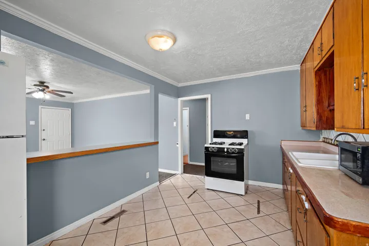 Kitchen featuring tile flooring, wood-finish cabinetry, a white gas range, and a pass-through window to an adjacent room