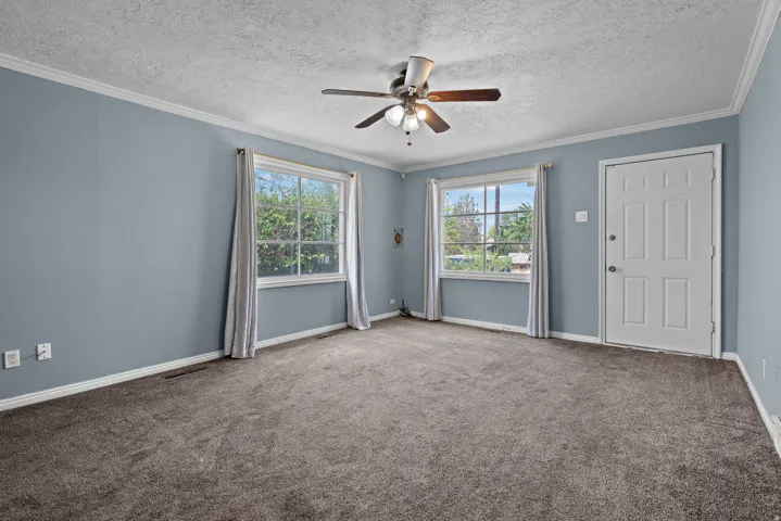 Spacious interior room featuring two large windows, a ceiling fan, and a paneled entry door