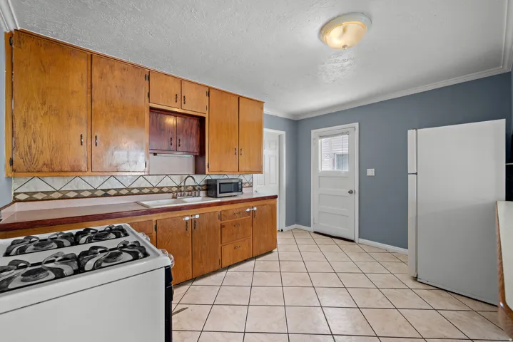 Kitchen featuring extensive wood cabinetry, tile flooring, a tile backsplash, and a white refrigerator