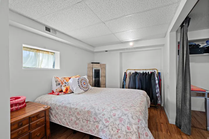 Room featuring wood-finish flooring, a rectangular window, a corner stone-clad element, and a ceiling with acoustic panels