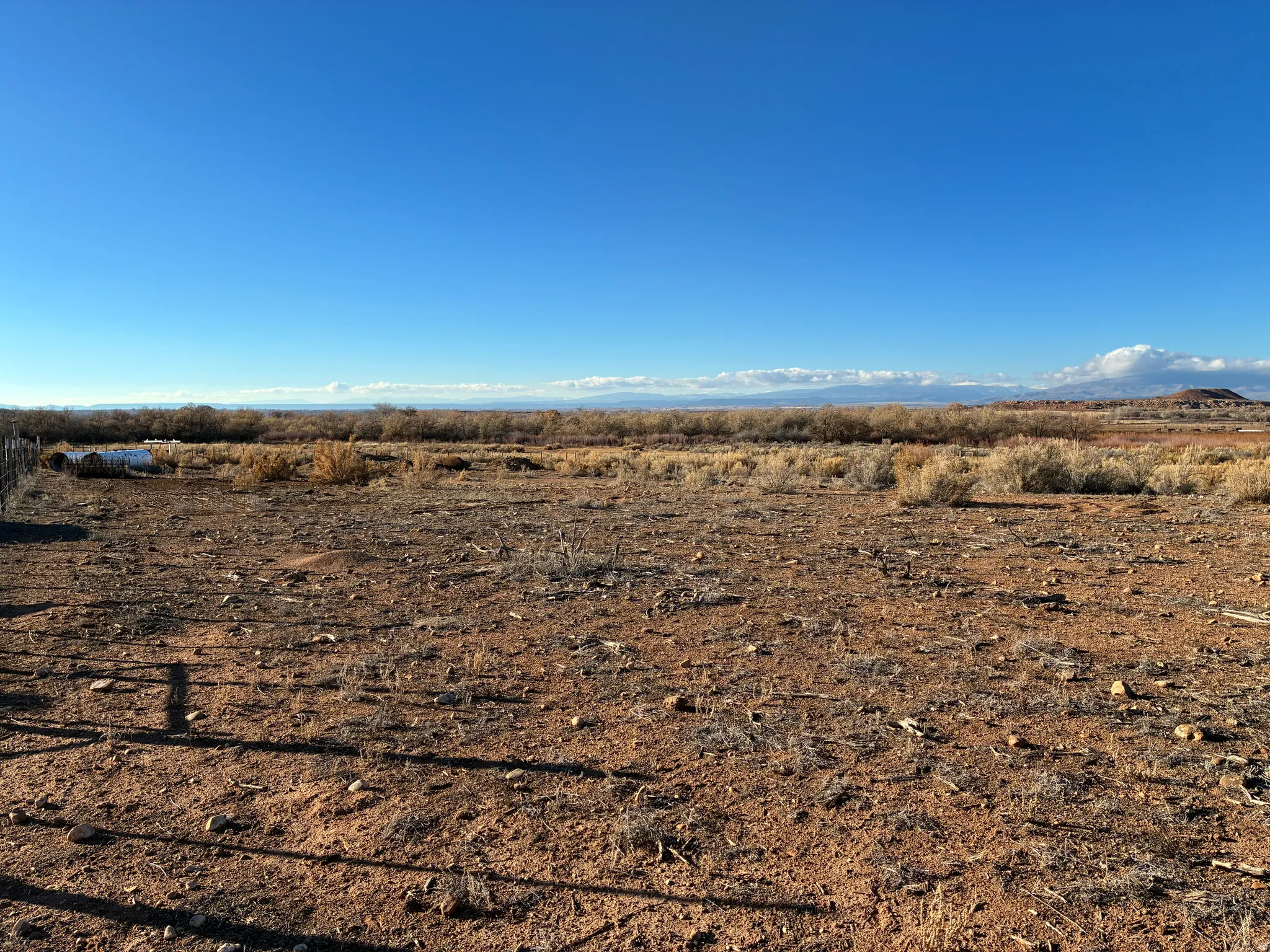 Expansive open land featuring sparse, dry vegetation and a distant body of water
