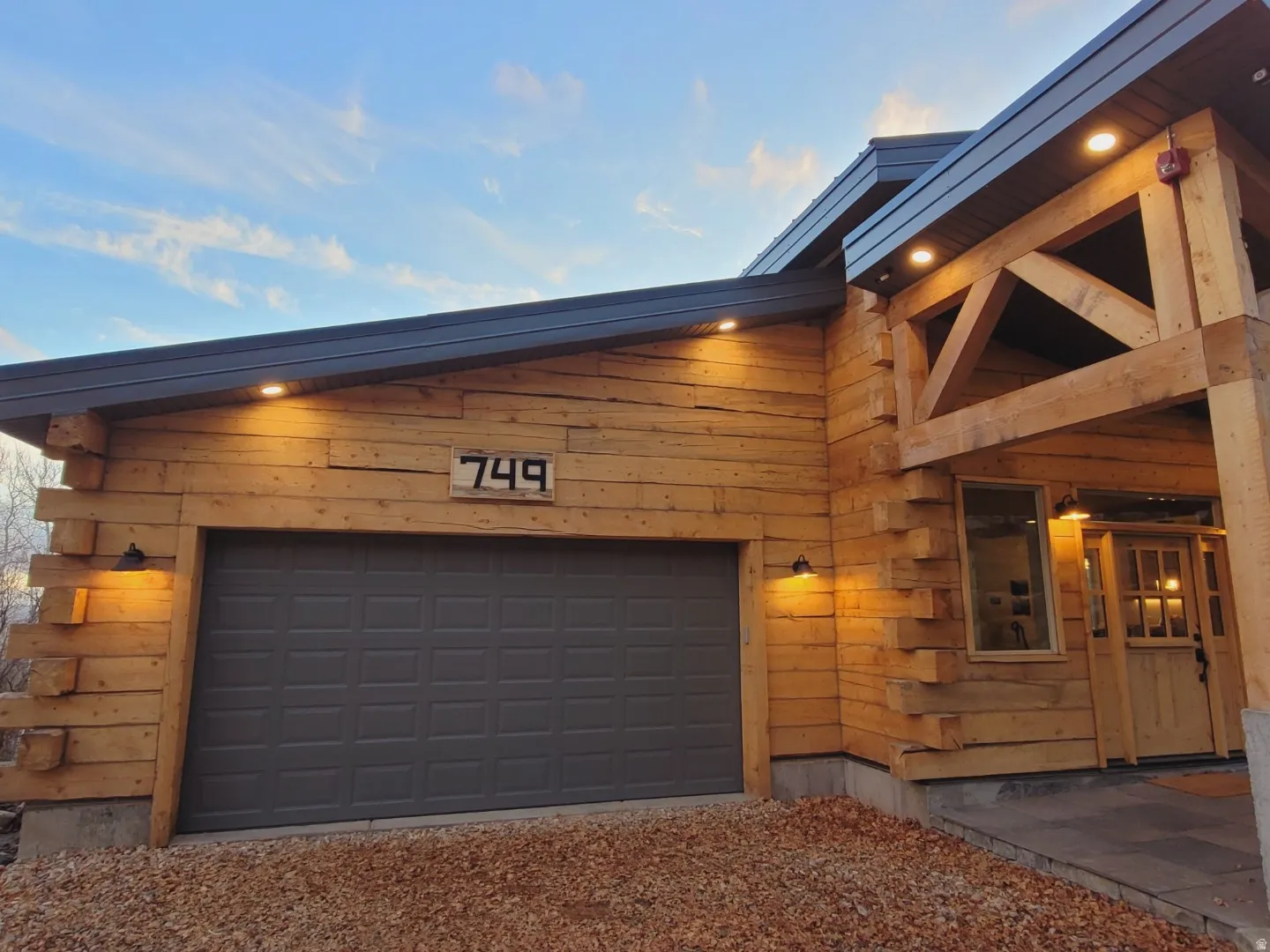 Exterior featuring log construction, a dark gray paneled garage door, exposed timber framing, recessed soffit lighting, and a distinct front entry door
