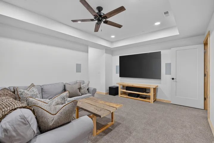 Media room featuring an entertainment wall with integrated speakers, tray ceiling with recessed lighting, and a dark wood-finish ceiling fan