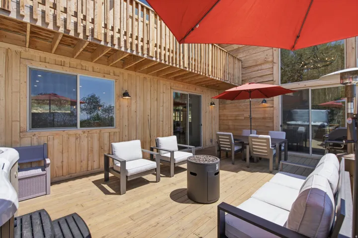 Expansive outdoor deck featuring natural wood decking, board and batten siding, multiple glass sliding doors, and barn-style exterior lighting