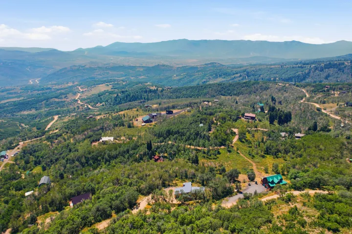 Expansive elevated terrain featuring scattered residential structures, mature green foliage, distant mountain ranges, and meandering unpaved roads
