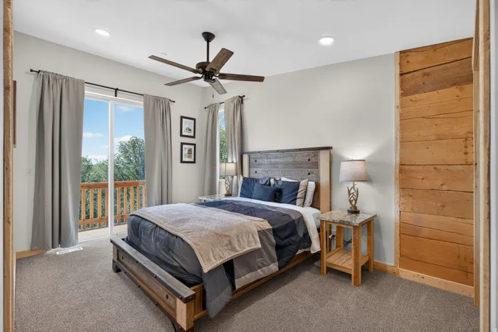 Sliding glass doors opening to a wood-railed balcony, recessed lighting, and a dark-toned ceiling fan