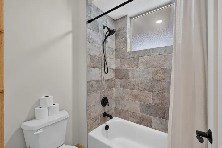 Bathroom featuring a tiled shower surround, recessed window, dark bronze fixtures, and a white bathtub