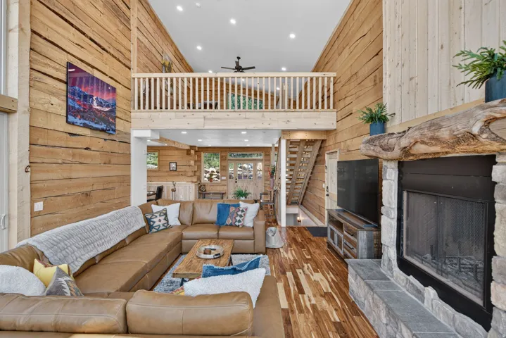Soaring wood-paneled great room with double-height ceilings, exposed timber beams, and a mezzanine-level loft space