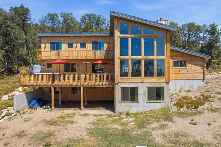Contemporary wood-sided residence featuring a multi-level deck, expansive floor-to-ceiling windows, an angled roofline, and a prominent chimney