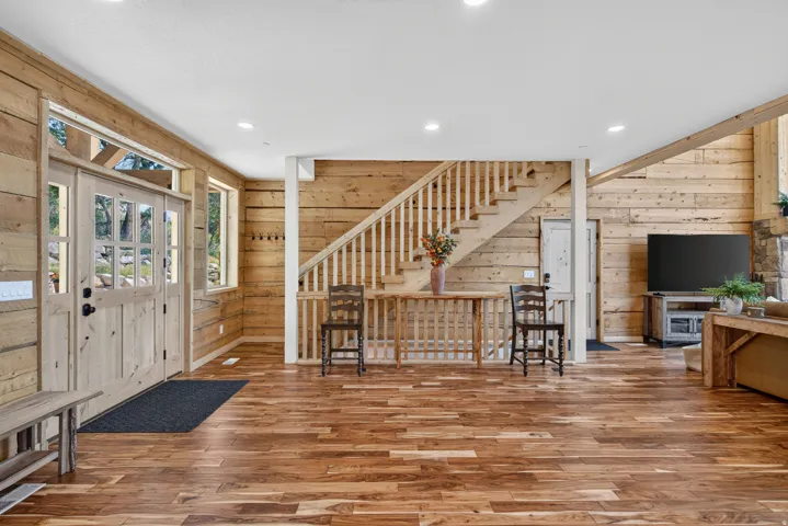 Spacious interior featuring wood-finish flooring, natural wood plank walls, and a prominent staircase with wood railings
