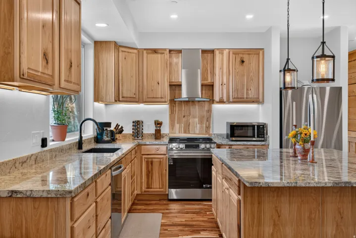 Kitchen featuring wood cabinetry, stone countertops, stainless steel appliances, and a central island with pendant lighting
