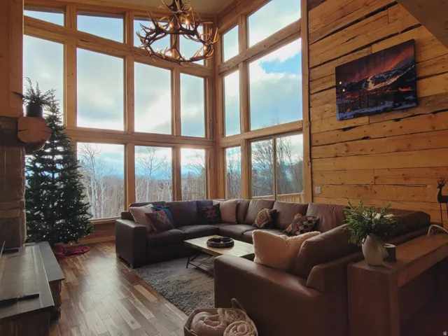 Two-story great room featuring a grand antler chandelier, expansive window wall, wood-finish flooring, and natural wood plank walls