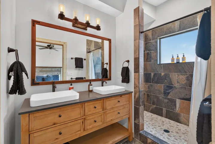 Double vanity with vessel sinks, wood-finish cabinetry, and dark countertop