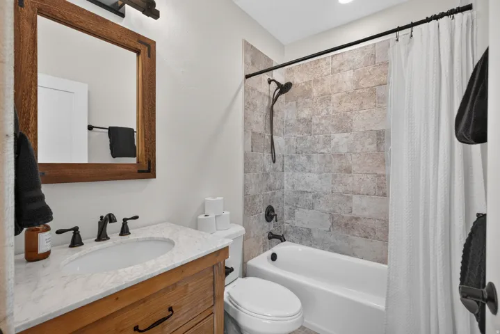 Bathroom featuring a wood vanity with an undermount sink and a light-toned countertop, a framed mirror, and a tiled shower surround with a tub
