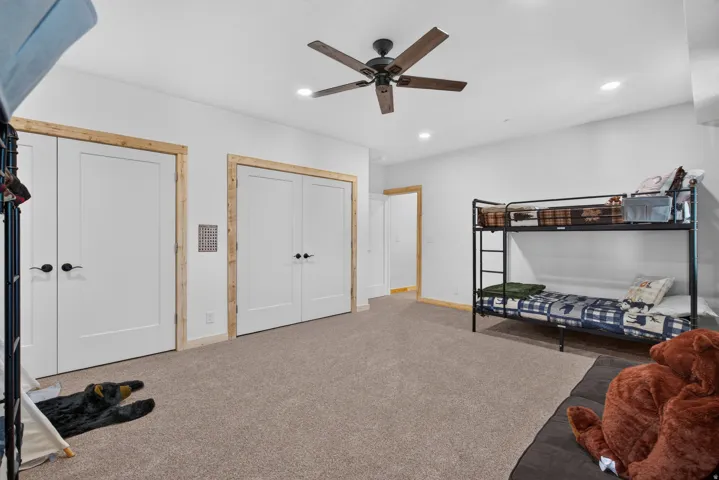 Spacious room featuring neutral carpet flooring, recessed lighting, a ceiling fan with wood-finish blades, and multiple white panel doors with natural wood trim