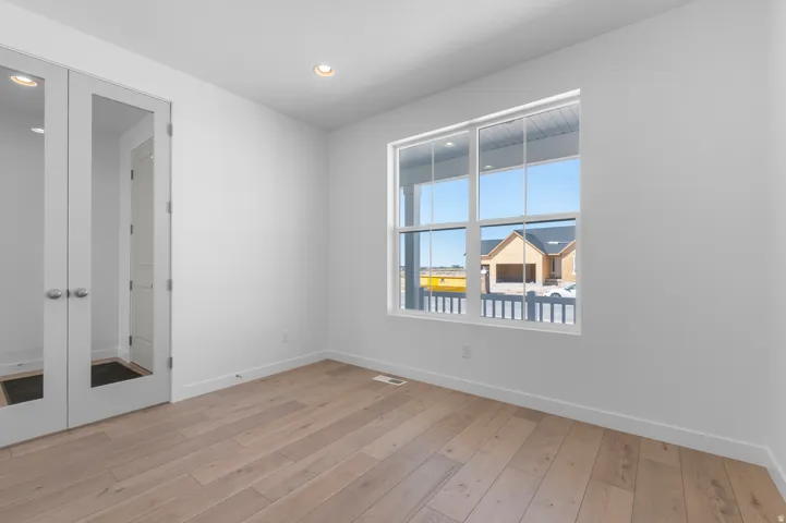 Recessed ceiling lighting, wood-finish flooring, white trim, dual glass-panel doors, and a multi-pane window