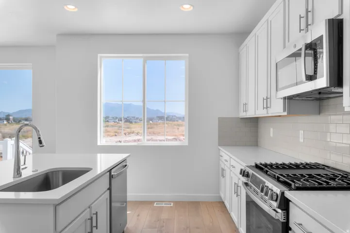 Kitchen featuring white cabinetry, stainless steel appliances, light wood-finish flooring, white countertops, and subway tile backsplash
