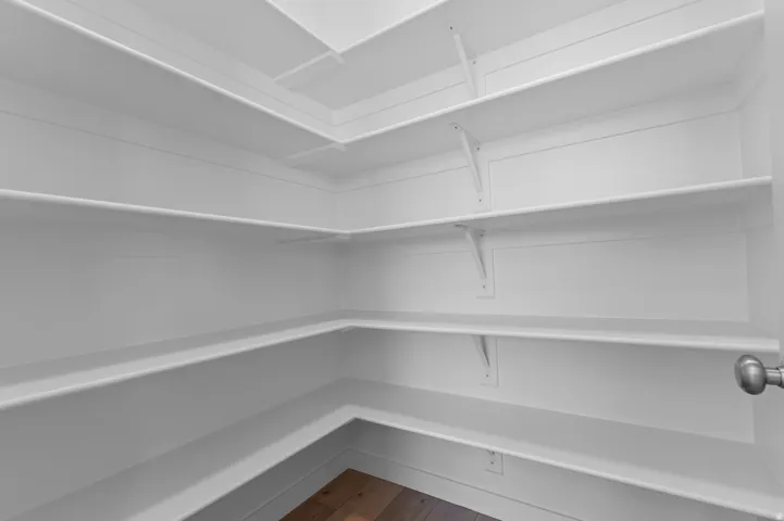 Walk-in pantry featuring white shelving, wood-finish flooring, and a brushed nickel door knob
